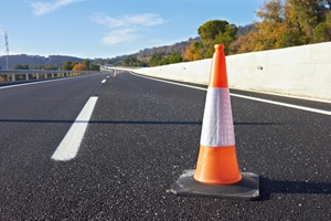 A close-up of an orange and white traffic cone placed on an empty highway, possibly after a car accident NSW, with a clear sky and trees in the background. A close-up of an orange and white traffic cone placed on an empty highway, possibly after a car accident NSW, with a clear sky and trees in the background.