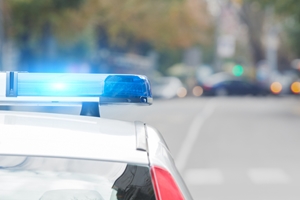 Close-up of a police car with blue lights flashing, parked on a blurred city street with trees and cars in the background, highlighting ongoing conversations about police brutality.