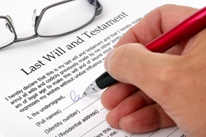 A hand holding a pen signs a "Last Will and Testament" document, with a pair of eyeglasses resting nearby—highlighting the importance of considering any potential family provision claim.