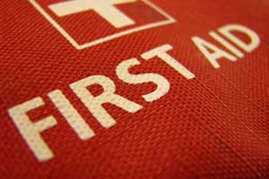 Close-up of a red first aid kit with a white cross and "FIRST AID" printed in bold white letters on the textured fabric, essential for workplaces handling work-related injuries claims.