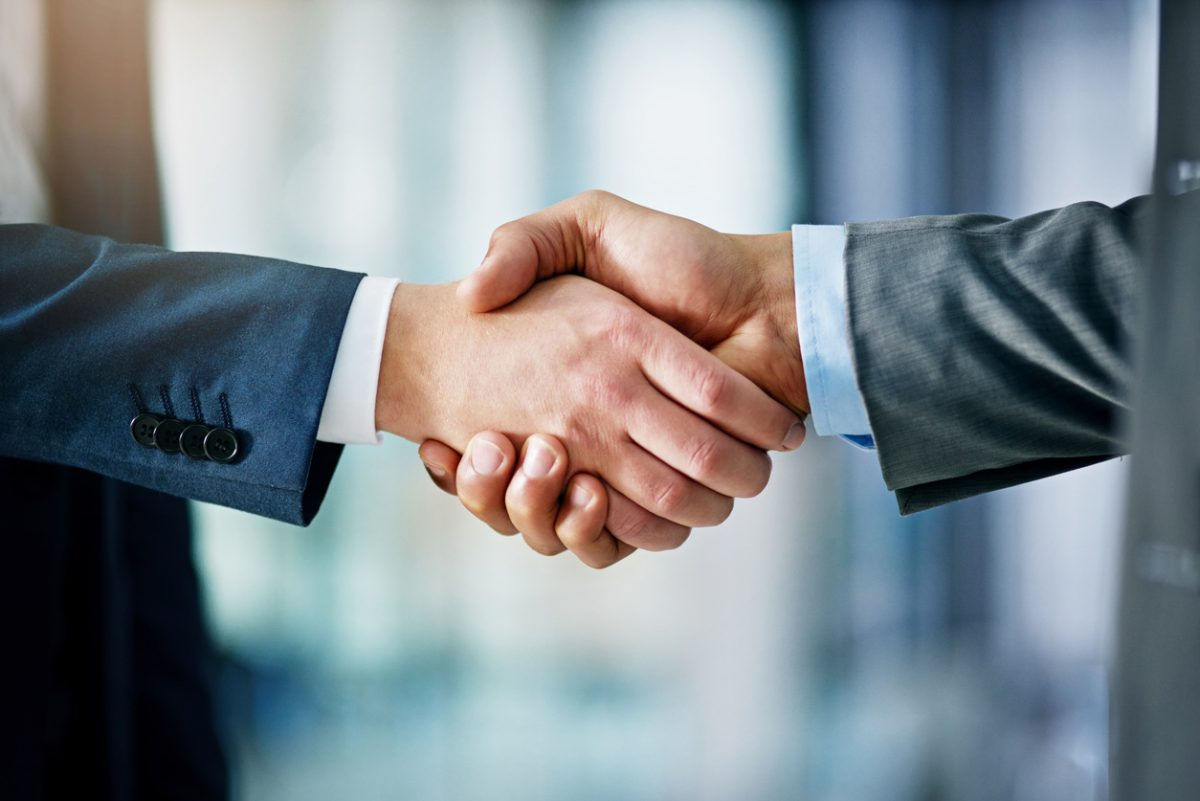Two people in business suits shaking hands, symbolizing agreement or partnership, with a blurred office background.