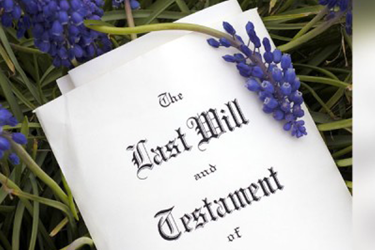 A document titled “Last Will and Testament” lies on green grass with purple grape hyacinth flowers resting on top.