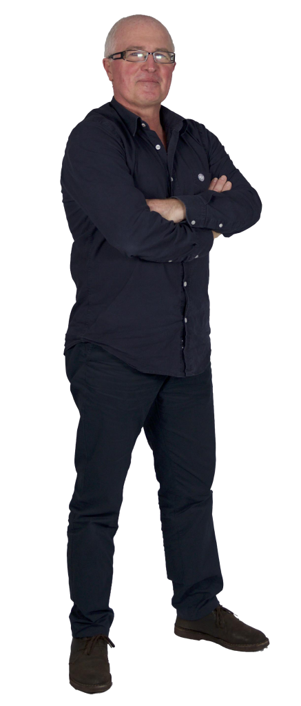 A man with short gray hair and glasses stands with his arms crossed, wearing a dark button-up shirt, dark pants, and brown shoes, facing forward with a neutral expression.