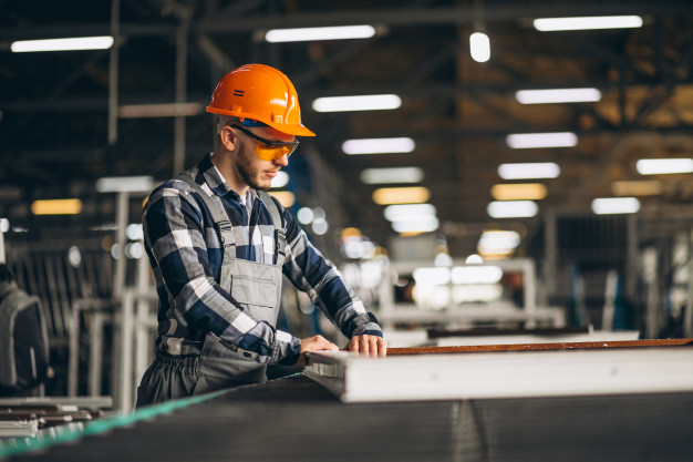 Worker Compensation A man wearing a hard hat and safety glasses operates machinery on a production line, highlighting workplace safety.