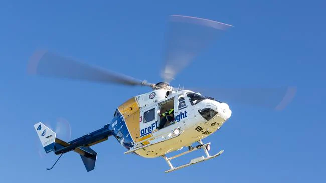 A white and blue rescue helicopter with "areflight" branding is flying against a clear blue sky, with its rotors in motion.